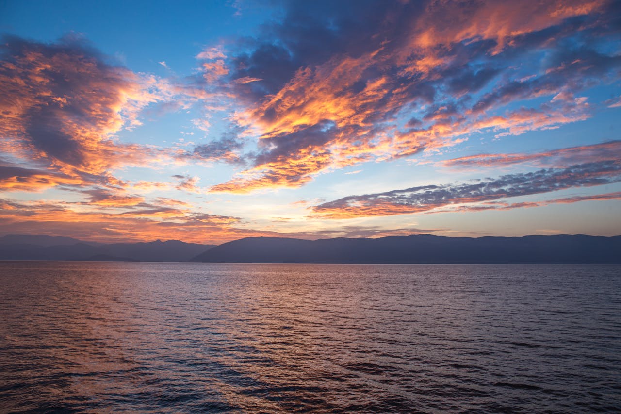 A vibrant sunset with dramatic clouds reflects over the calm ocean, capturing natures beauty.